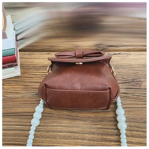 Detail of a brown leather mini bag with a bow accent and large white pearl strap
