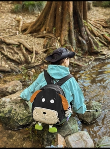 Outdoor shot of the cartoon dog-shaped black nylon backpack with cute 3D ears and green paws