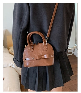 Back view of model wearing a brown shell-shaped crossbody bag with decorative bow