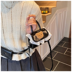 Detail of black mini crossbody bag featuring white lace trim and 3D plush bear motif