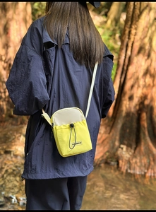 Detail of yellow and beige nylon crossbody bag with drawstring pocket in forest setting