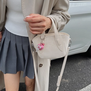 Dettaglio borsa a mano in pelle crema con ciondolo a cuore e accessorio chiave argento