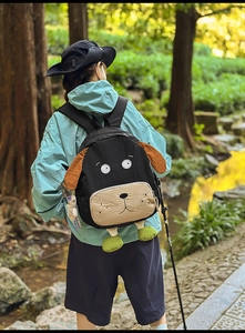 Outdoor view of the cute black puppy-shaped backpack featuring 3D brown ears and green feet