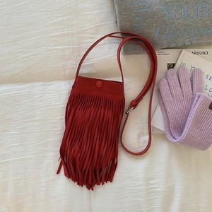 Détail d'un sac bandoulière rouge à franges en daim avec accessoires d'automne