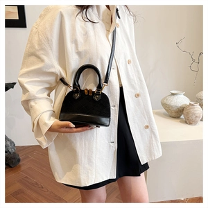 Close-up of black shell handbag with gold zipper and leather strap on model