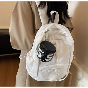 Detail of white nylon backpack with a black mini bucket bag pendant showing embroidery
