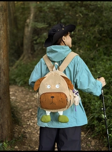 Detail of cute puppy-shaped khaki backpack with 3D ears and plush pendant in forest