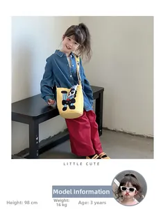 Yellow canvas kids bucket bag with cartoon dog print and striped strap worn by a girl