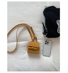 Mini mustard yellow square crossbody bag next to a smartphone showing its compact size