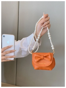Mini orange PU leather bag with pearl handle and bow detail compared to phone size