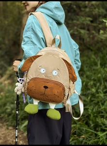 Detailed view of beige puppy backpack with brown ears and plush feet in forest setting