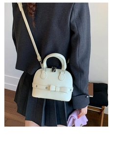 Detail view of cream shell crossbody bag with leather bow on a model for size perspective