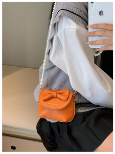 Detailed view of an orange mini crossbody bag with a large bow and pearl strap