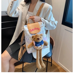 Detail of cute white backpack with brown plush bear charm worn by a model in a white suit