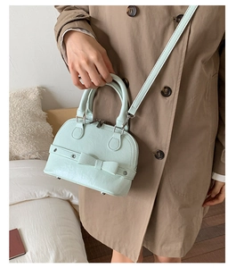 Detail of mint green shell bag featuring elegant bow decor and sturdy round handles
