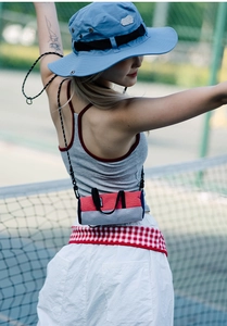 Outdoor scene showing a nylon cylinder crossbody bag and a light blue sun hat on a tennis court