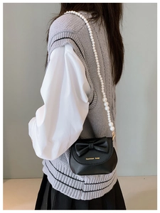 Detail of a mini black crossbody bag with bow decoration and elegant pearl strap