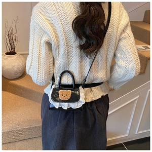 Detail of a mini black crossbody bag with a cute plush bear head and white lace trim