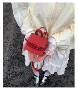 Detail view of a mini red square handbag with metal buckle held by model on road