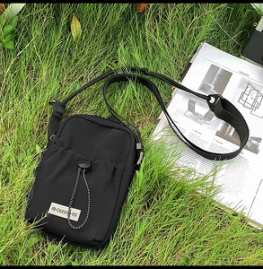 Detail view of black nylon crossbody phone bag with drawstring pocket on green grass