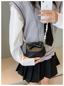 Mini black crossbody bag with bow detail and pearl chain worn by a child model