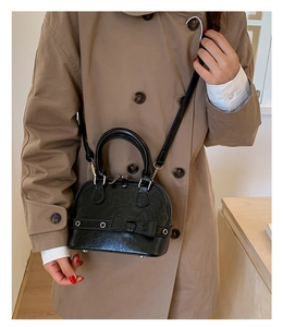 Detail of black shell bag with bow and silver eyelets shown on khaki trench coat