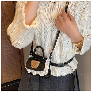 Girl wearing black patent leather bag with brown plush bear patch and white lace trim