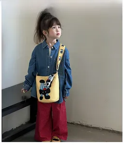 Close-up of cute yellow canvas crossbody bag for kids with cartoon dog print worn by model