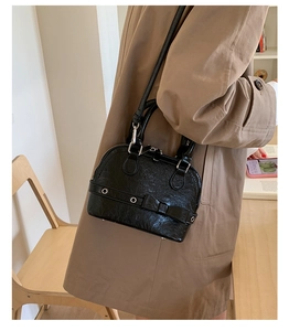 Detail of black shell bag with bow and silver studs worn with a classic beige trench coat