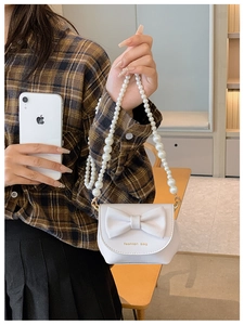 Detail of white mini handbag with large bow and elegant pearl beaded crossbody strap