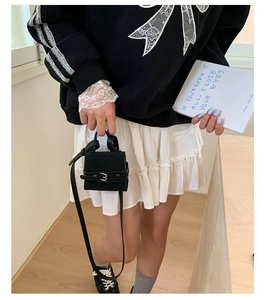 Detailed shot of black mini crossbody bag with silver buckle on a stylish model