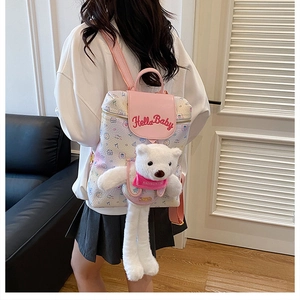 Detail of pink cartoon backpack featuring Hello Baby embroidery and a white teddy bear charm