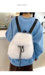 Rear view of a white faux fur backpack with black straps worn by a model in casual style