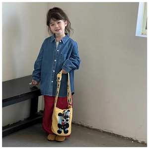 Detail of child wearing blue denim shirt and yellow canvas bucket bag with animal embroidery