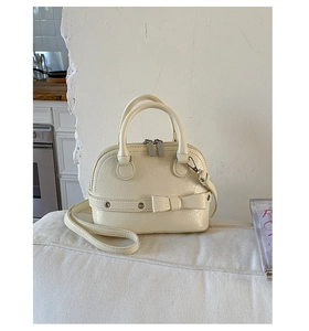 Detail of cream shell bag featuring decorative bow, silver eyelets, and metallic hardware