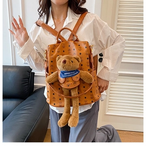 Detailansicht eines braunen Lederrucksacks mit einem Plüschbären und blauem Schal