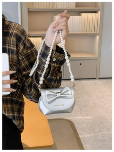 Detail of silver mini girl's bag with large bow, pearl strap, and gold fashion bag text