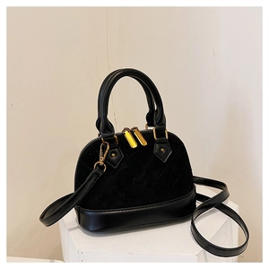 Close-up of black quilted shell handbag with gold hardware on minimalist white stand