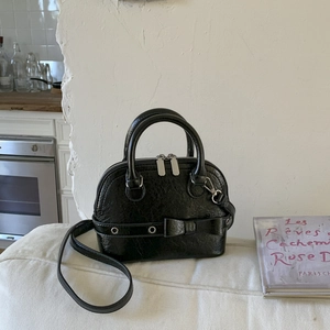Close-up of black pleated texture shell bag with bow detail and silver metal eyelets
