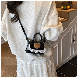 Detail view of mini plush bear crossbody bag with white lace trim on black shiny fabric