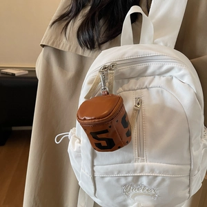 Brown mini cylinder coin purse with heart detail hanging on a white backpack
