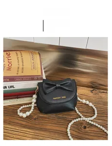 Detail of mini black leather handbag with large bow and pearl beaded strap on a wooden table