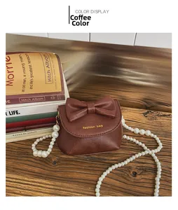 Detail of coffee brown mini handbag with pearl chain and bow on wooden table