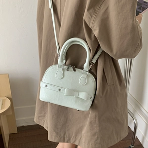 Side view of mint green shell bag worn with a brown coat in a minimalist setting