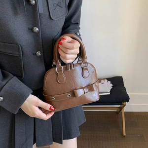 Brown shell bag with bow detail held by model in professional suit, lifestyle view