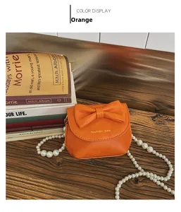 Detail of orange mini PU leather purse with bow decoration and pearl chain on wood table