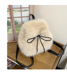 Detail of plush off-white backpack featuring a cute black drawstring bow on a wooden surface