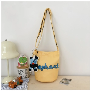 Detail of yellow bucket bag with elephant print, shoulder strap and plush elephant charm