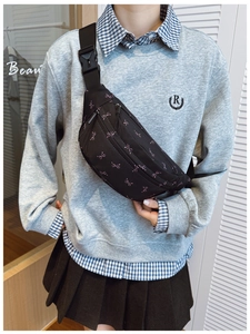 Close-up of black crossbody bag with pink bow pattern and adjustable strap on model