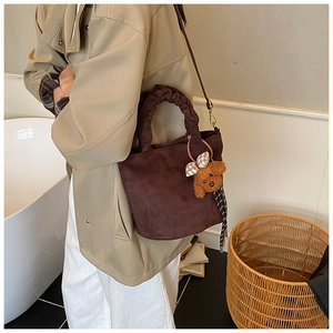 Detail of a brown suede tote bag featuring ruffled handles and a cute plush bear charm